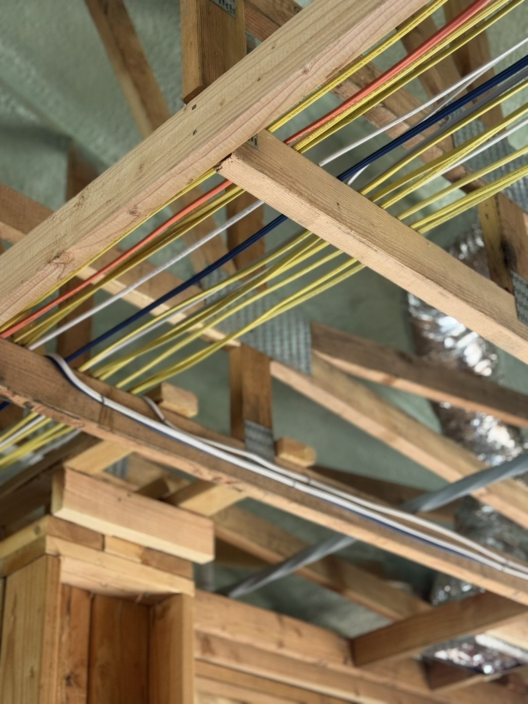 Attic electrical rough - color-coded runs across the trusses