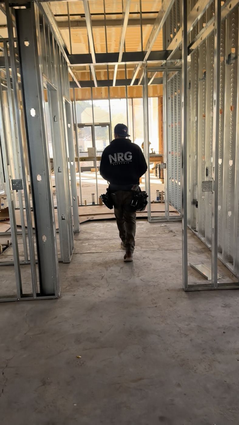 NRG electrician walking metal-stud framed commercial interior