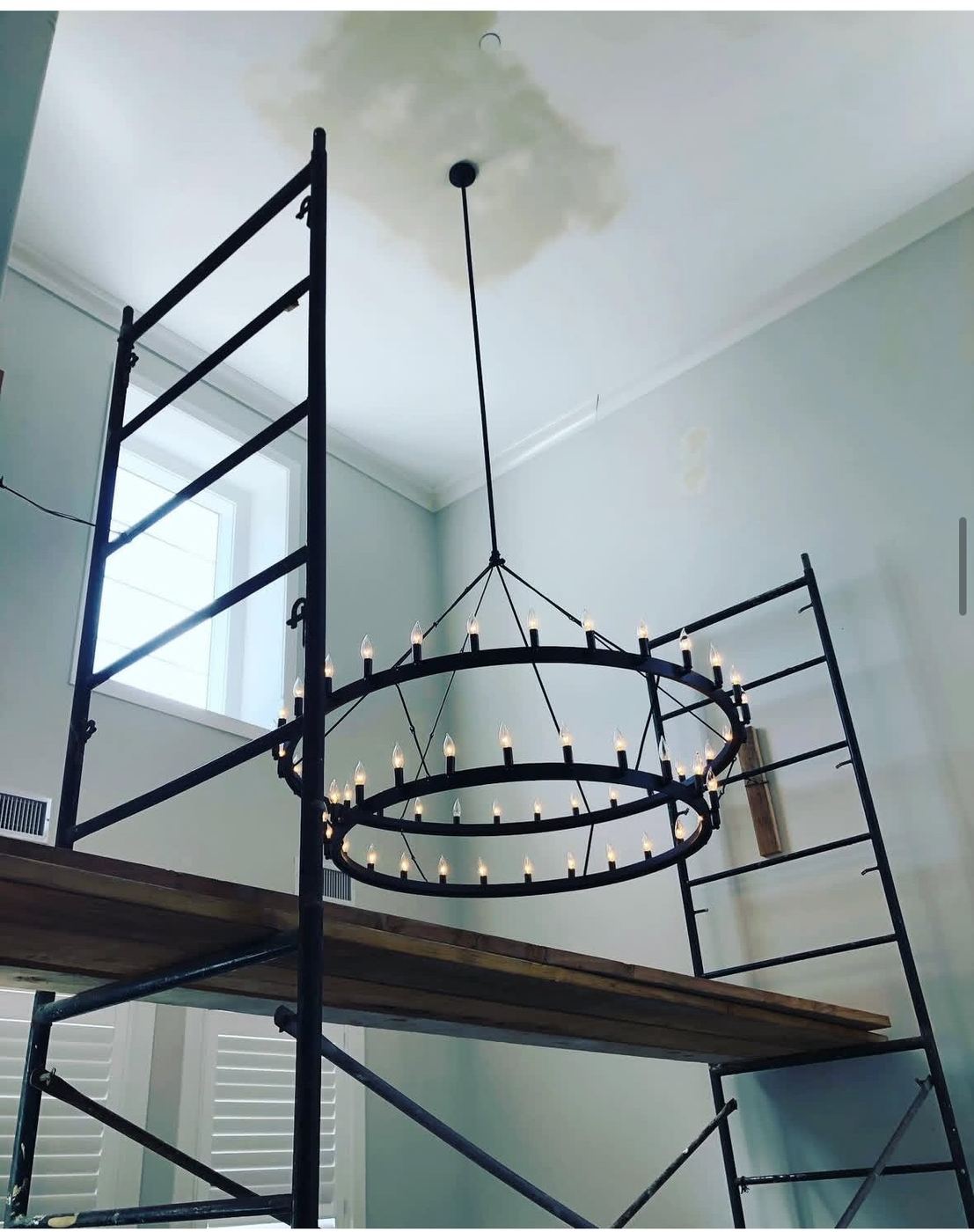 Ring chandelier going up from scaffold in a high-ceiling room