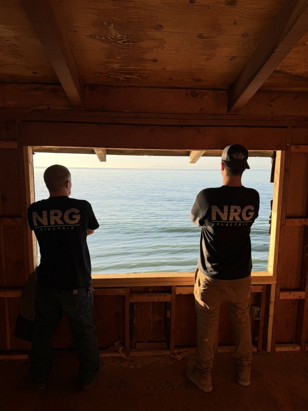Two NRG Electric crew at a framed ocean-view window opening