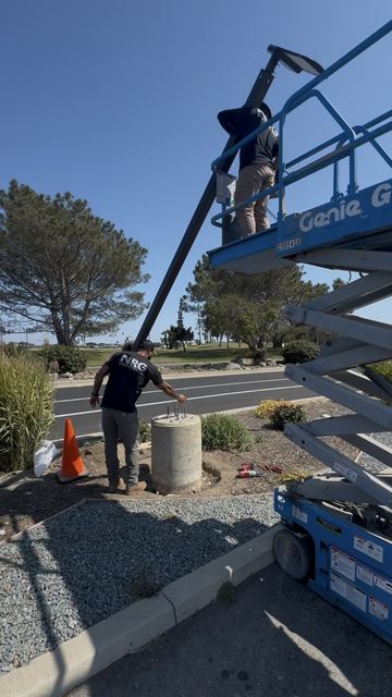 NRG crew setting a parking-lot light pole with a scissor lift near the beach