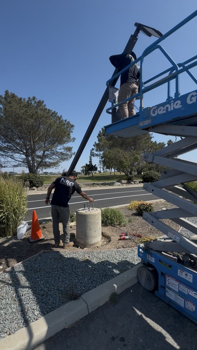 NRG crew setting a parking-lot light pole with scissor lift near the beach
